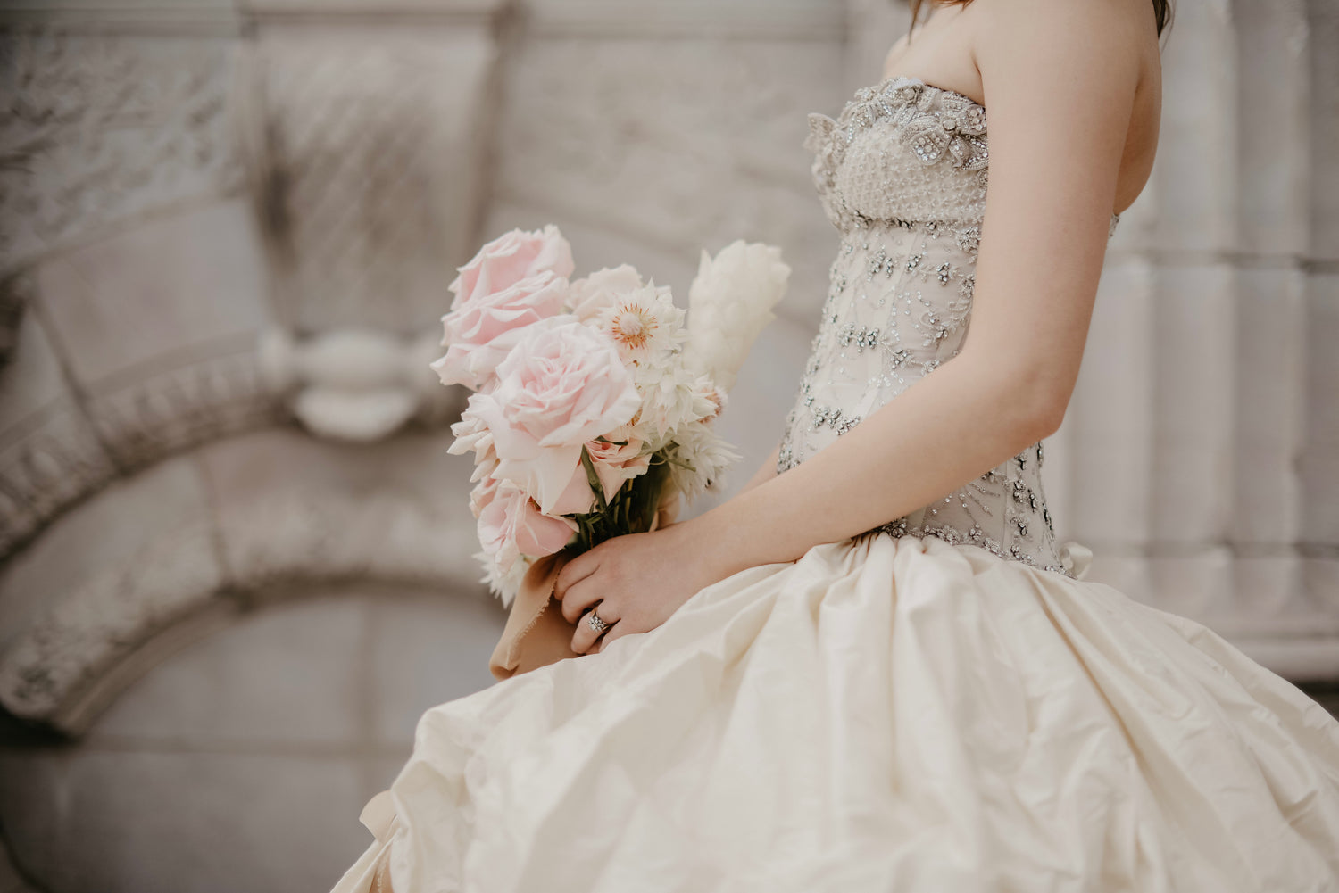 detailed wedding dress, bride holding a bunch of flowers with her engagement and wedding ring on