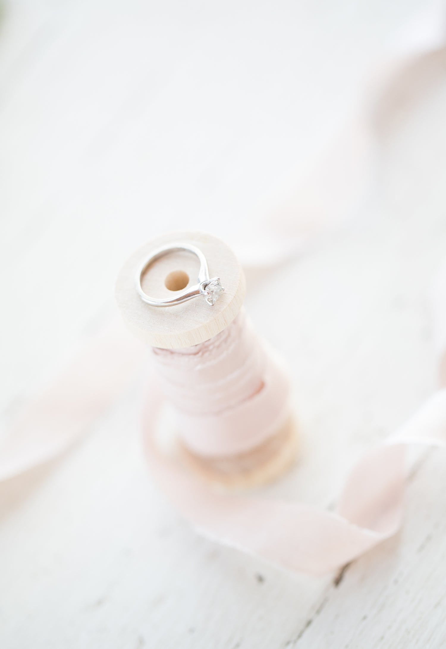 engagement ring on a wooden spool with pink ribbon